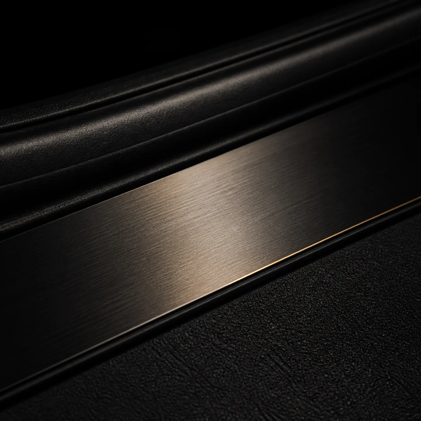 A brushed metal door sill plate with a thin brass edge line, below black door trim.