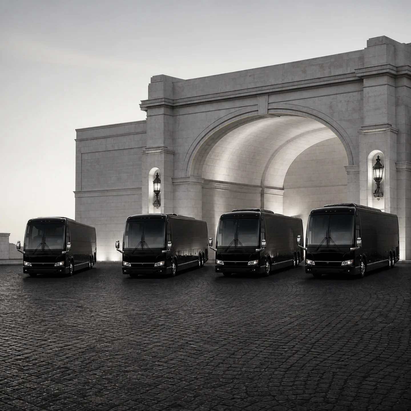 Four black Prevost H3-45 motorcoaches parked nose-out in a fanned arc before a stone archway entrance at dusk.